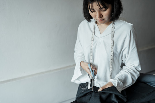 年轻的亚洲女设计师在展厅里用剪刀剪原布——制作服装。