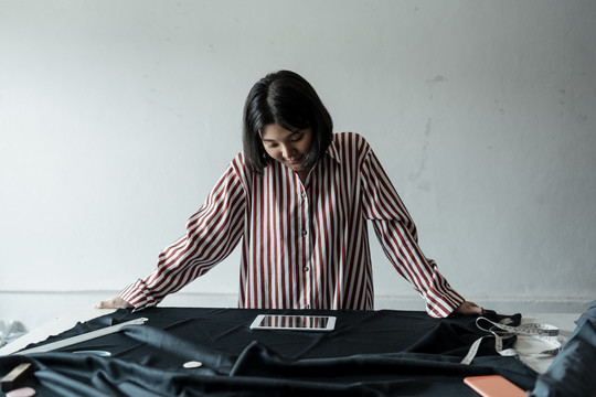 年轻的亚洲女设计师看着平板电脑在工作台上寻找信息。