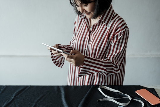 一位年轻的亚洲设计师手持平板电脑在展厅里做衣服。