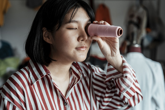 年轻的亚洲设计师，拿着粉色的线，假装它像望远镜。