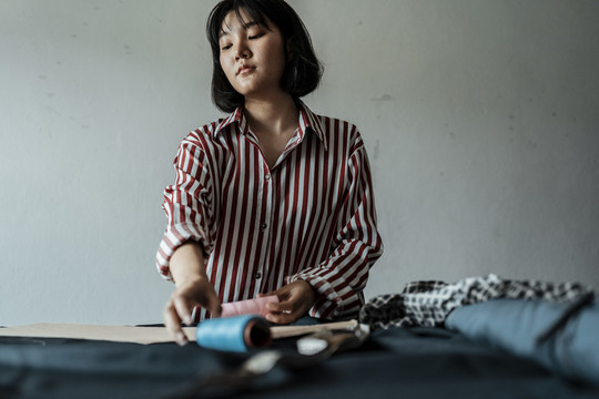 年轻的亚洲女设计师用粉笔石刮布，在展厅里做衣服。