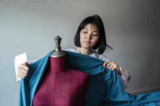 年轻的亚洲设计师短发女人用蓝色的生布盖住假人。德西格在做她的项目。
