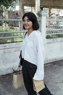 穿着白衬衫的亚洲年轻女子拿着购物纸袋走在街上。