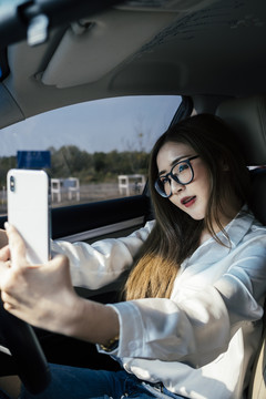 交通和车辆概念-戴眼镜的泰国妇女用智能手机在车内自拍。