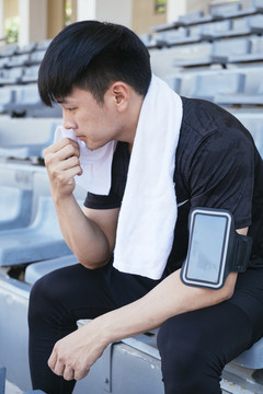 运动亚泰男子在黑色运动服挂毛巾在脖子上休息坐在椅子上在体育场。