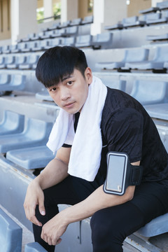 运动亚泰男子在黑色运动服挂毛巾在脖子上休息坐在椅子上在体育场。