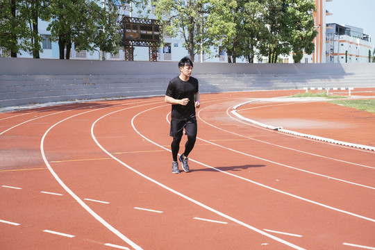 运动亚泰男子身穿黑色运动服慢跑或在体育场内跑道上跑步。
