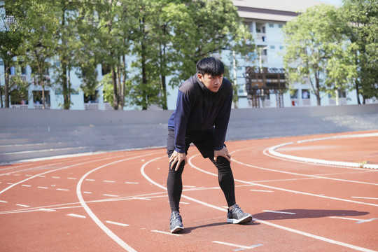 一名身穿黑色运动服的亚泰男子在体育场内的跑道上跑步后休息了一会儿。