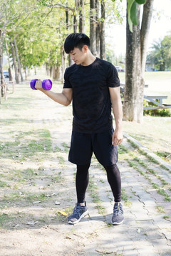 运动亚泰男子穿着黑色运动服使用紫色哑铃在公园。我在锻炼。