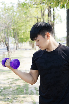 运动亚泰男子穿着黑色运动服使用紫色哑铃在公园。我在锻炼。