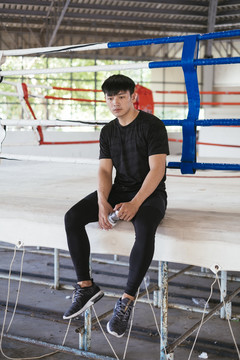 身穿黑色运动服的亚泰男子在拳击场外休息。