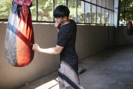 运动亚泰男子穿黑色运动服练习泰拳沙袋。拳打脚踢。