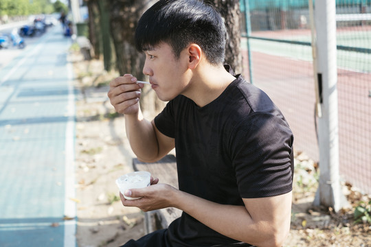 运动亚泰男子身穿黑色运动服，运动后吃健康的谷类酸奶。