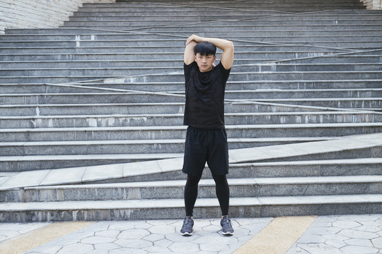 亚泰男子穿黑色运动服伸展手臂热身前锻炼。