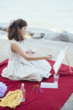美丽的亚泰艺术家在夏天的海滩上用白色的衣服在画布上作画。