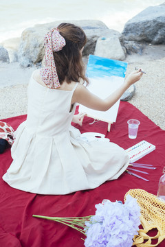 后视图-美丽的亚泰艺术家在沙滩上的卡瓦斯画白色礼服。