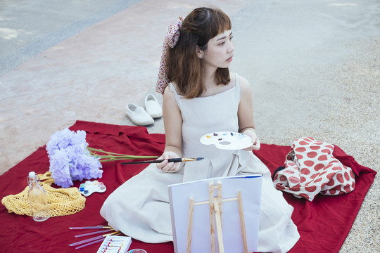 美丽的亚泰艺术家在户外用小画笔在画布上画白色连衣裙。