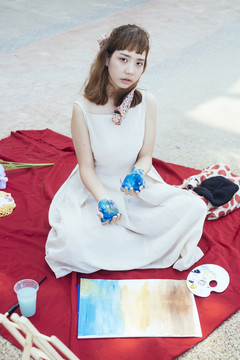 美丽的亚泰艺术家在白色的衣服脏手蓝色。在红垫子上画画。