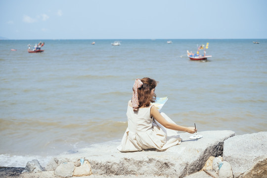 后视图-美丽的亚泰艺术家在白色的衣服画在海滩上的夏天。