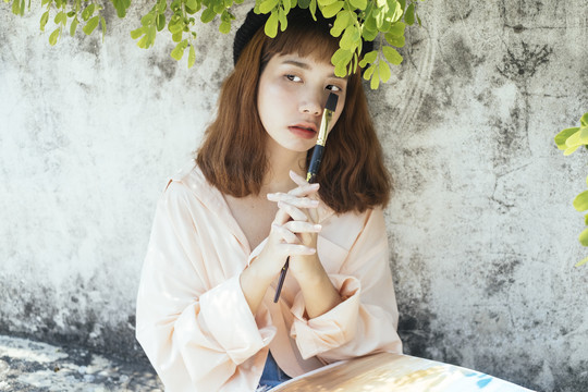 特写镜头美丽的新潮亚泰艺术家在白色礼服举行小油漆刷下树叶。