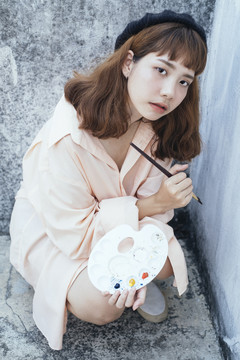 特写镜头美丽的新潮亚泰艺术家在长衬衫持有彩色画笔和调色板。
