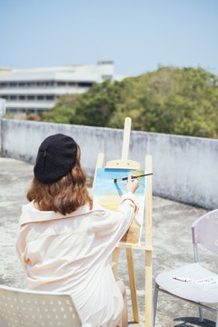 后视图-美丽的新潮亚泰艺术家在长衫油画与油漆刷户外屋顶地板。