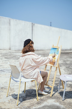 后视图-美丽的新潮亚泰艺术家在长衫油画与油漆刷户外屋顶地板。