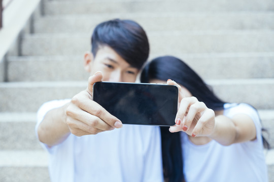 一对穿着白色t恤的情侣坐在鹅卵石楼梯上，互相取笑，展示智能手机屏幕。