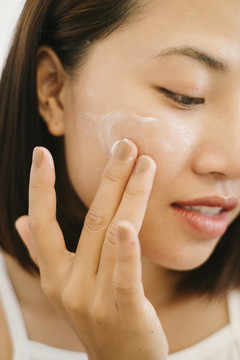 美丽的亚泰女人的特写黑色短发在脸上涂抹美容护肤霜。