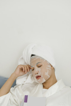 一个穿着白色浴袍的年轻女子躺在客厅的沙发上敷着化妆面具。