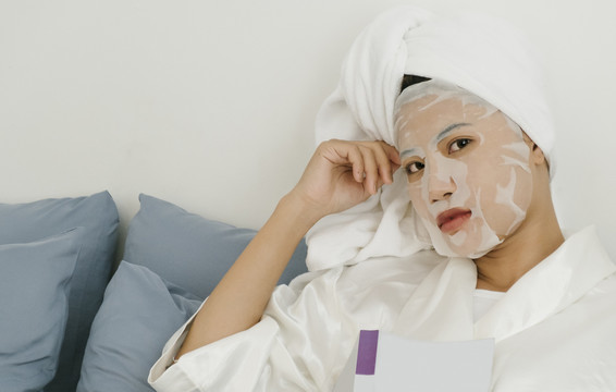 一个穿着白色浴袍的年轻女子躺在客厅的沙发上敷着化妆面具。