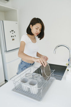 性感的亚泰女人穿着白衬衫在厨房的水槽里洗盘子。