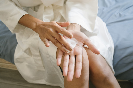 穿着浴袍的女人在卧室里用手涂护肤霜的手。