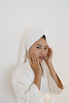 性感的亚泰女人穿着白色浴袍在脸上涂护肤霜隔离在白色背景下。
