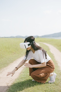 黑色长发女子穿着休闲服，戴着VR护目镜，在泥泞的草原上行走，享受虚拟现实技术。