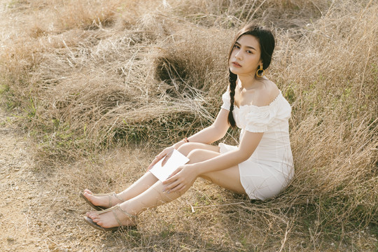 黑辫白衣女子坐在干涸的草原上，在阳光明媚的日子里举着方镜，全身舒展。