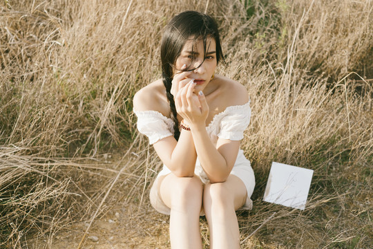 阳光明媚的日子里，黑辫子白衣女人坐在干燥的草地上，一面镜子。