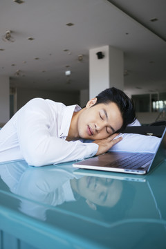 聪明的亚泰商人穿着白领衬衫睡在笔记本电脑前。厌倦了工作。