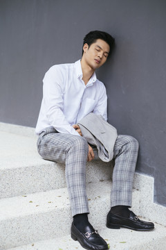 聪明的亚泰商人穿着白领衬衫坐在楼梯上休息，在户外睡觉。
