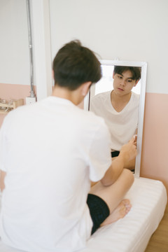 一个黑发男人空着脑袋坐在镜子前，他的指针指向镜子。
