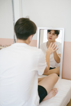 一个黑发男人空荡荡的坐在镜子前，用手触摸镜子。
