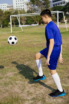 穿着蓝色足球服的男孩在田里踢足球的肖像。