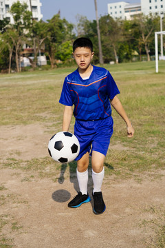 一个泰国男孩在操场上独自练习他的足球技术。