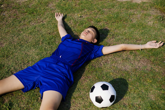 泰国男孩在练习足球后躺在草地上休息。