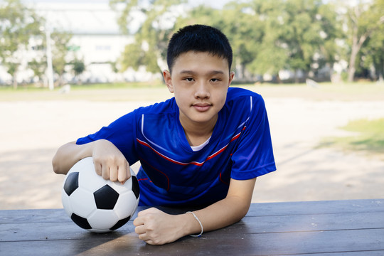 一个男孩在球场旁的木桌上踢足球的肖像照。