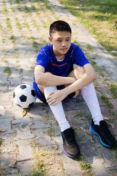 一个男孩拿着足球坐在人行道上。