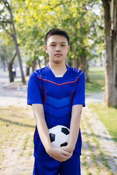 一个男孩站在公园的人行道上，手里拿着一个球。
