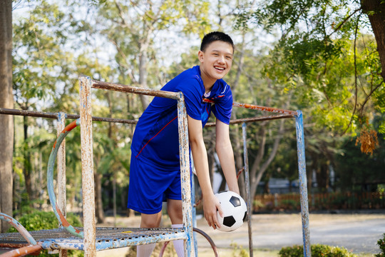 穿着蓝色套装的快乐男孩站在操场的攀爬架上，与足球水平。