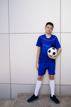 一个男孩拿着足球站在白墙边。