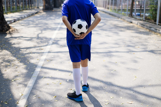 一个男孩背着足球走在学校的人行道上。